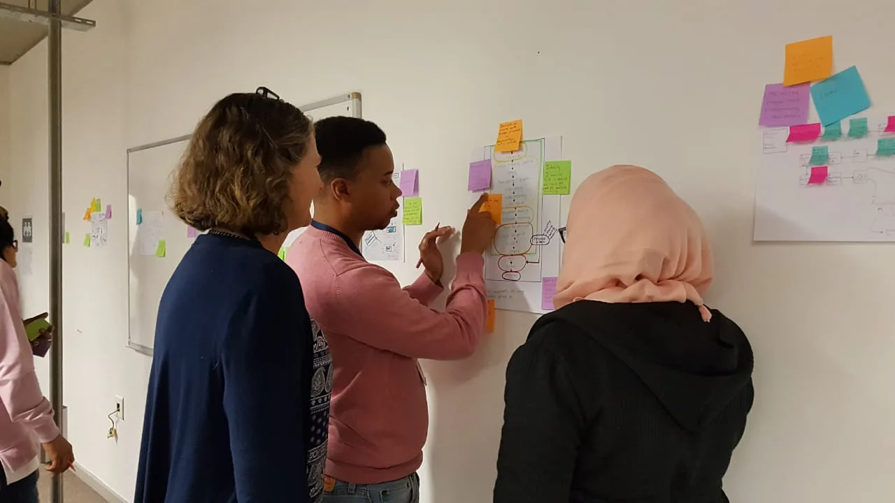 Varias personas examinan diagramas y notas adhesivas colocados en una pared durante un taller.