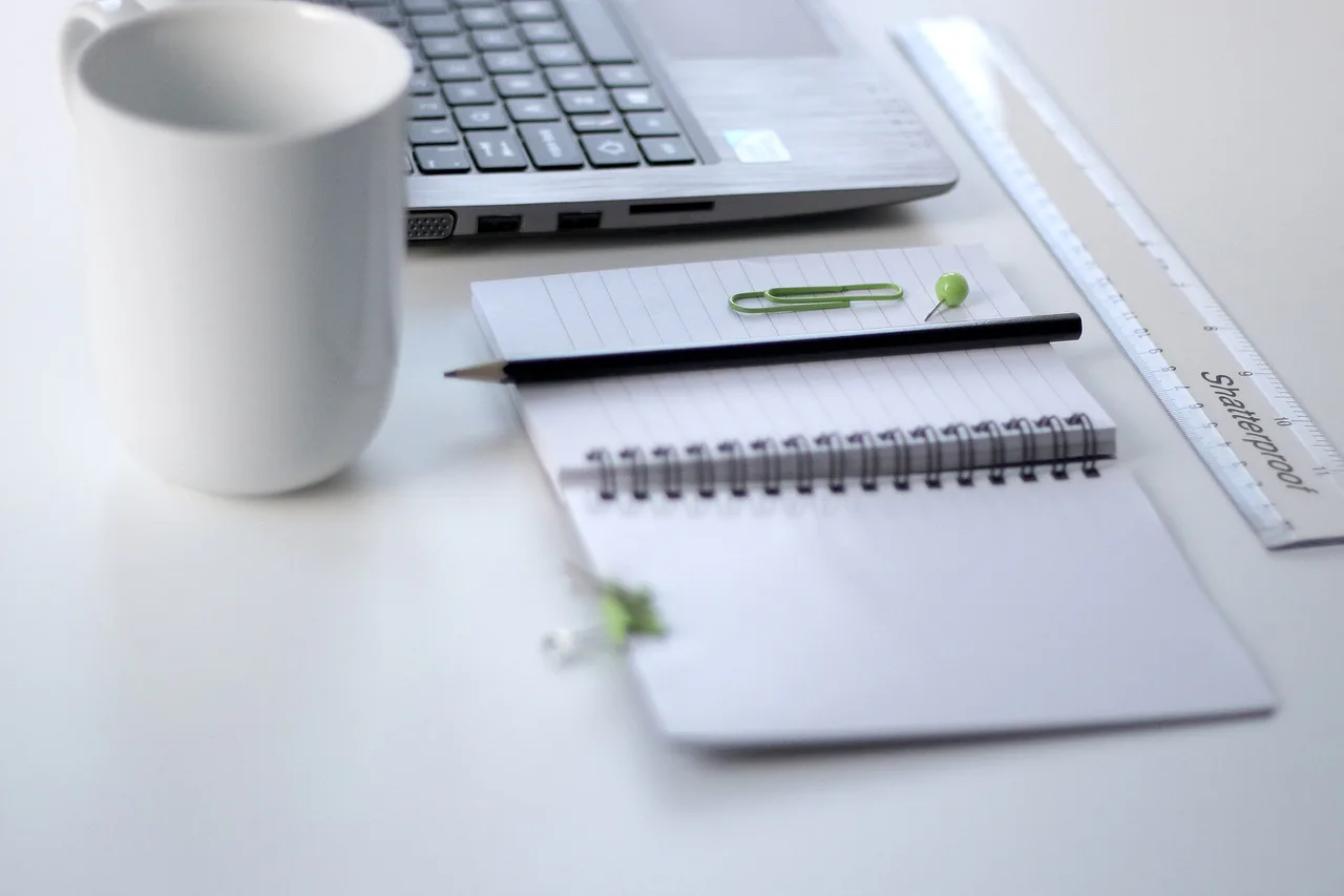 Cuaderno de espiral, lápiz y regla junto a un portátil y una taza