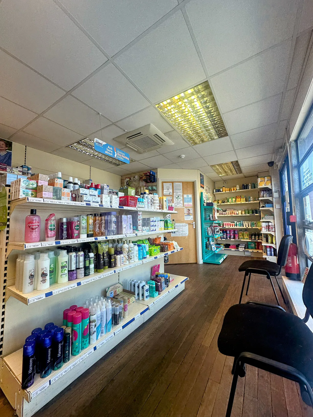 Estanterías con productos de cuidado personal y sillas en el interior de una farmacia.