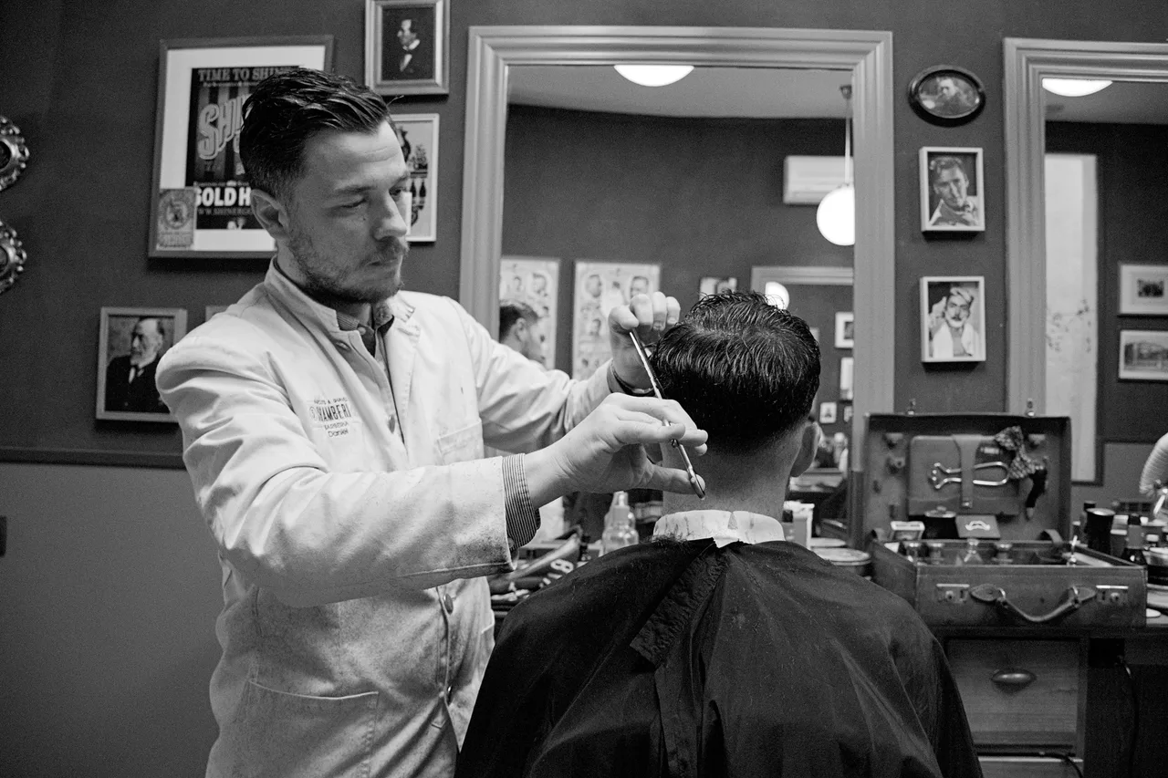 Un barbero corta el cabello de un cliente sentado frente a un espejo.