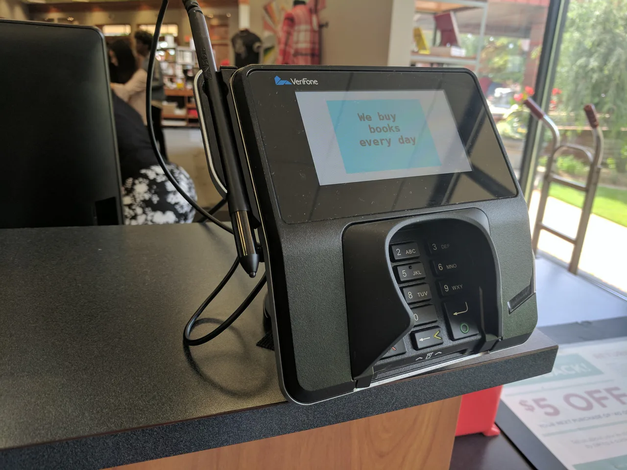 A payment terminal with a keypad and screen on a bookstore counter.