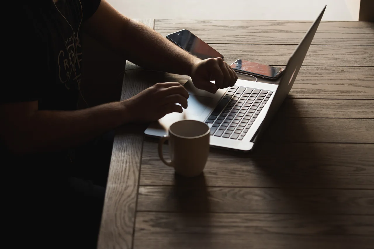 Persona trabajando con un portátil y dispositivos móviles sobre una mesa
