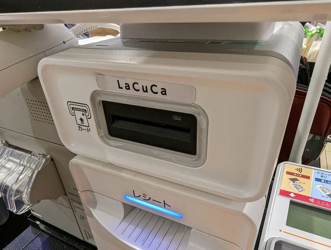 Lector de tarjetas LaCuCa con ranura y salida de recibos, junto a un terminal de pago en una caja