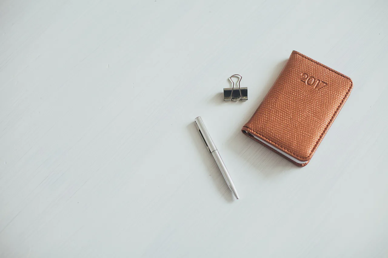 Cuaderno de cubierta marrón junto a un lápiz y una pinza
