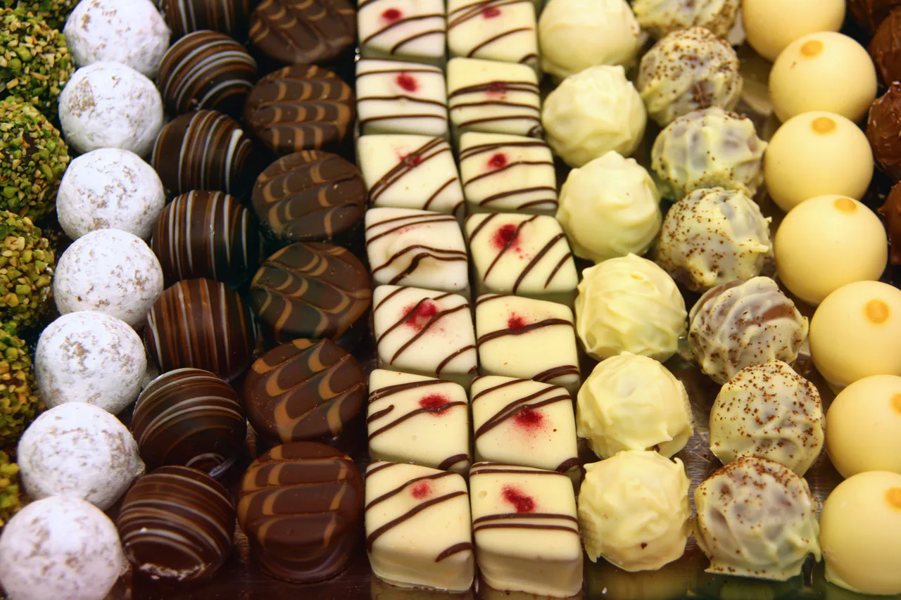 Rows of white, milk and dark chocolate pralines and truffles with different coatings and decorations