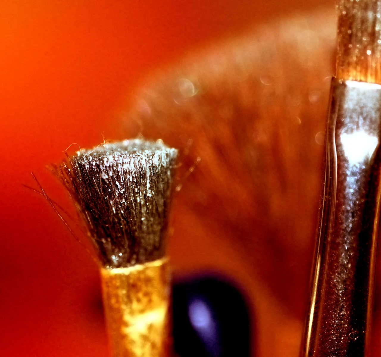 Close-up of a makeup brush with pale powder on its bristles against an orange background