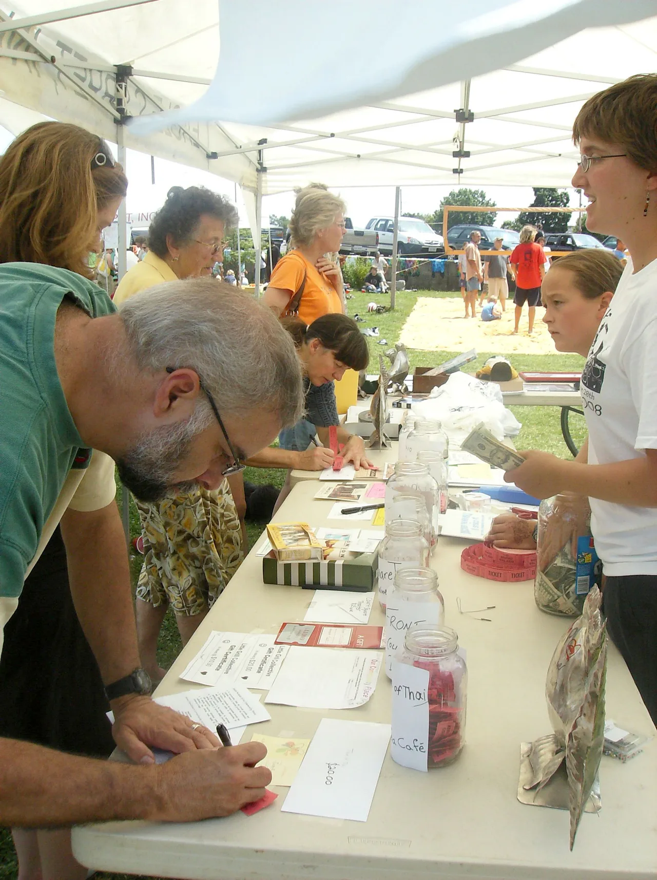 Personas completan formularios en una mesa de un sorteo comunitario al aire libre.