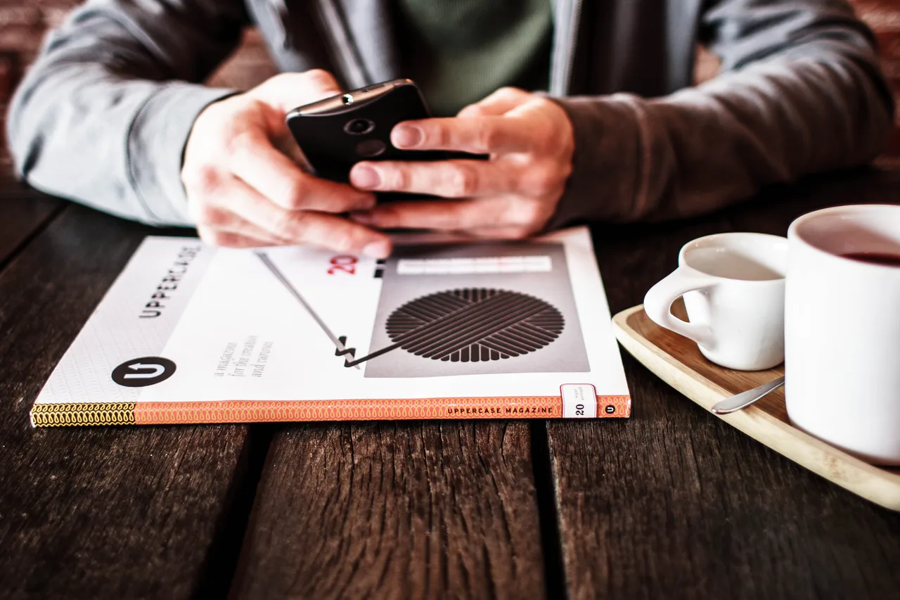 Person using a phone at a table with reading material