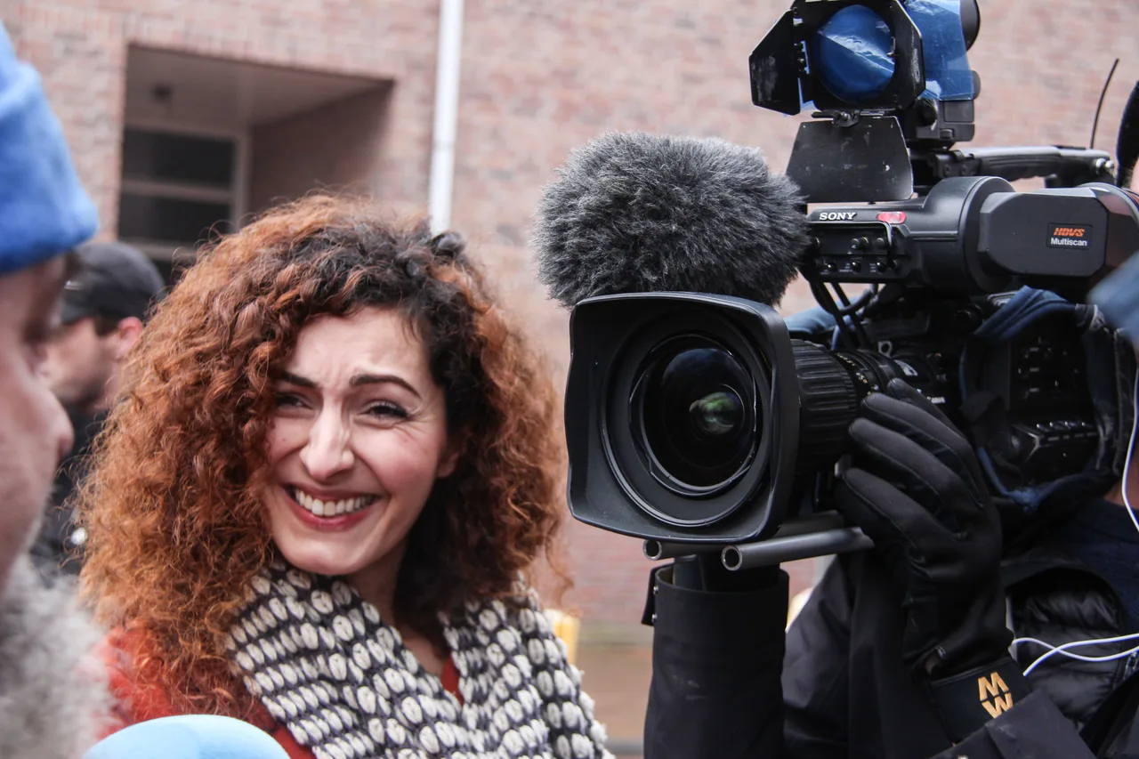A woman speaks beside a filming crew with a camera and microphone.