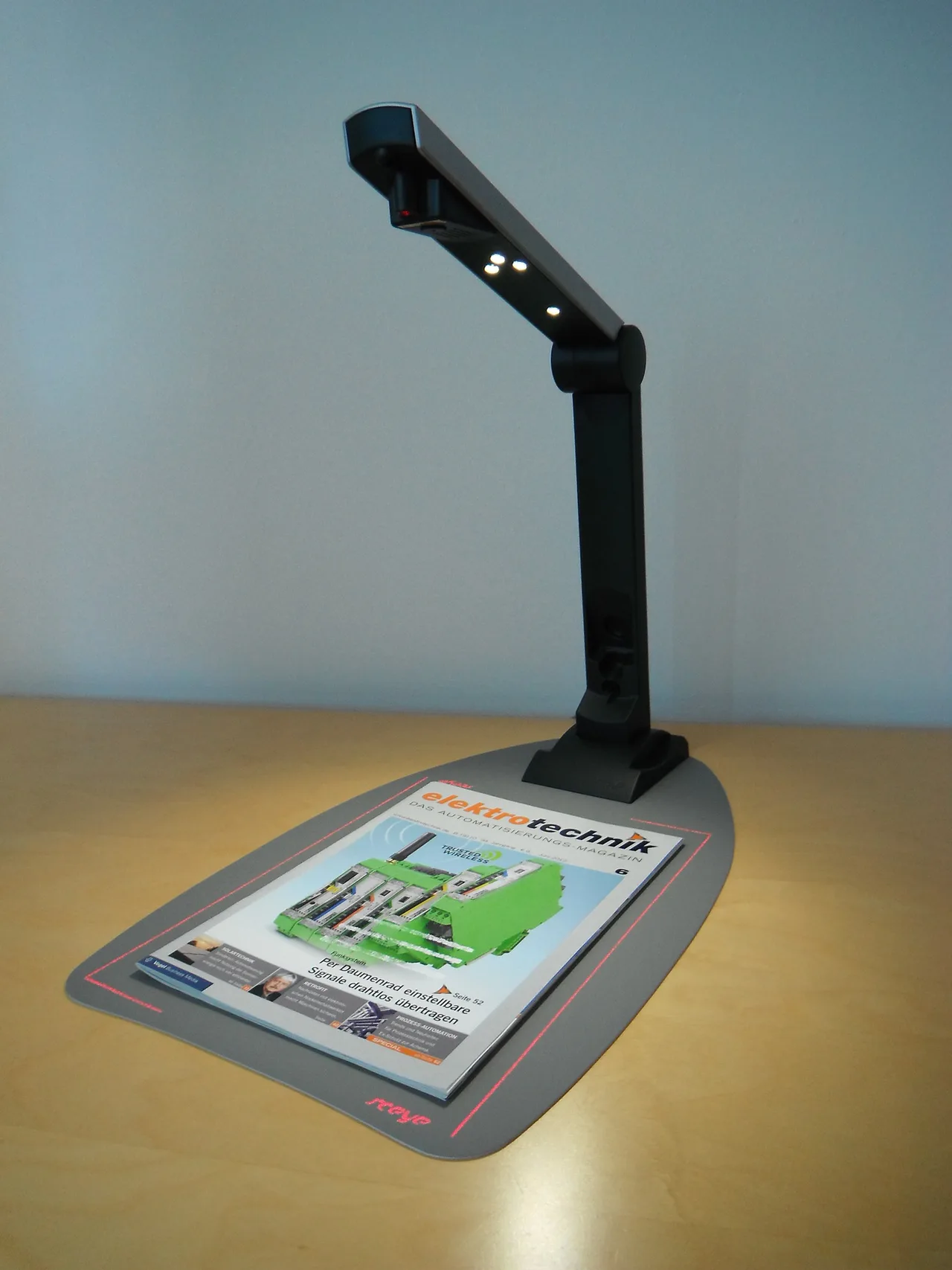 A sceyeX document scanner illuminates a magazine beneath its camera.
