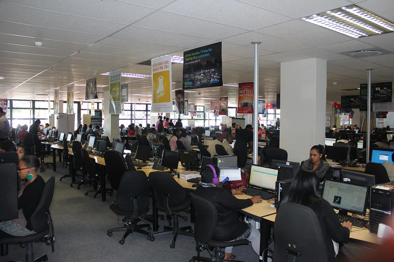 Personas con auriculares trabajan ante ordenadores en un centro de atención telefónica.