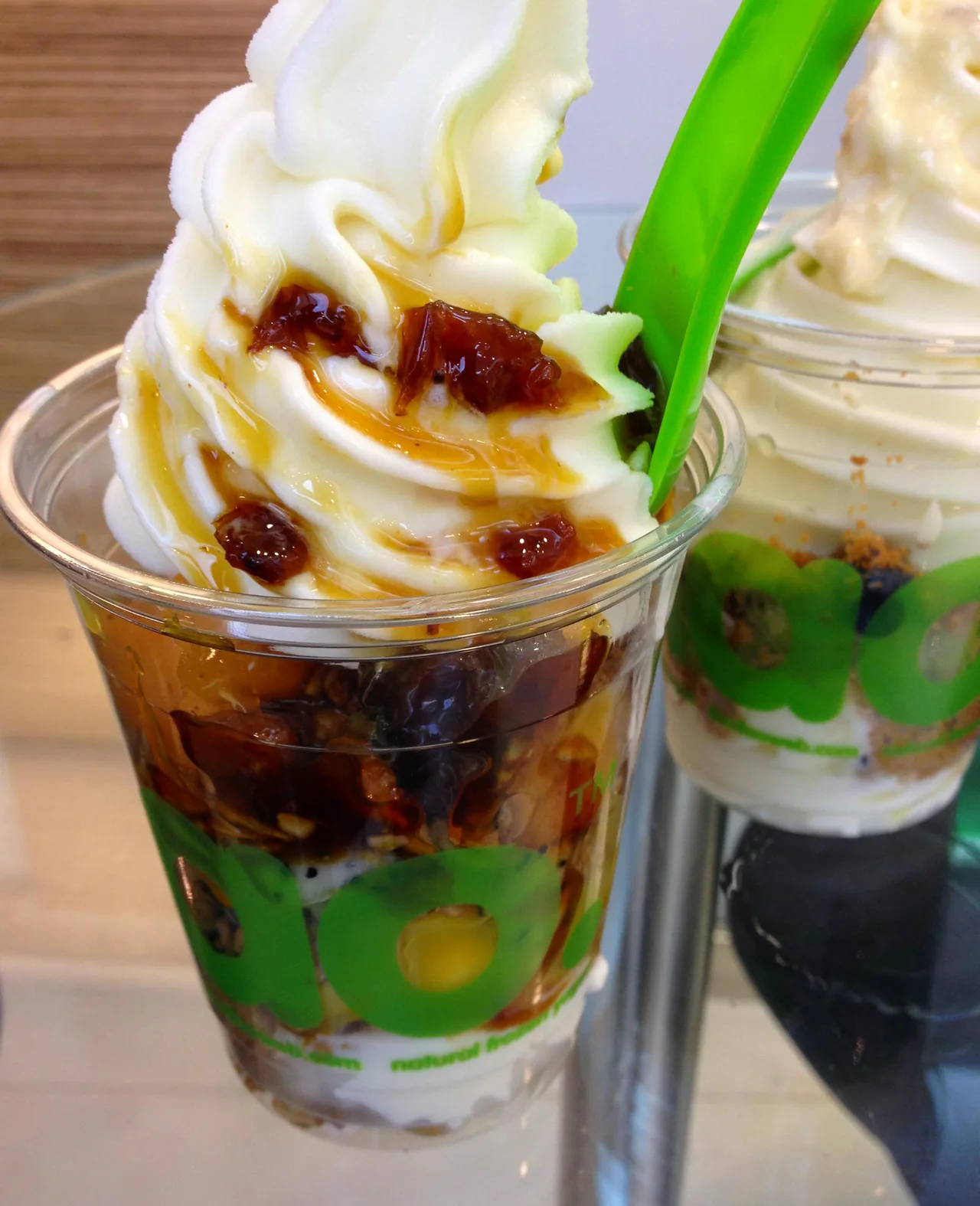 Two llaollao frozen-yogurt cups with toppings and green spoons in Singapore