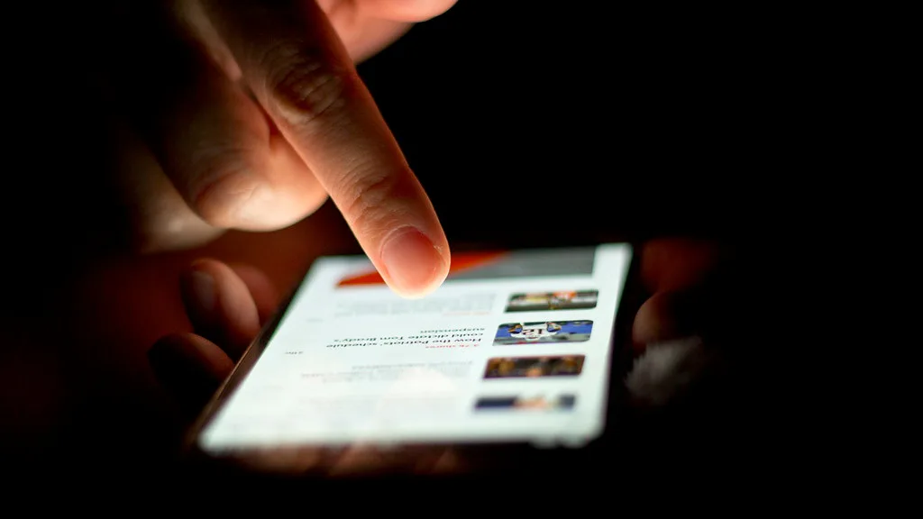 A person scrolls through a list of news stories on a phone.