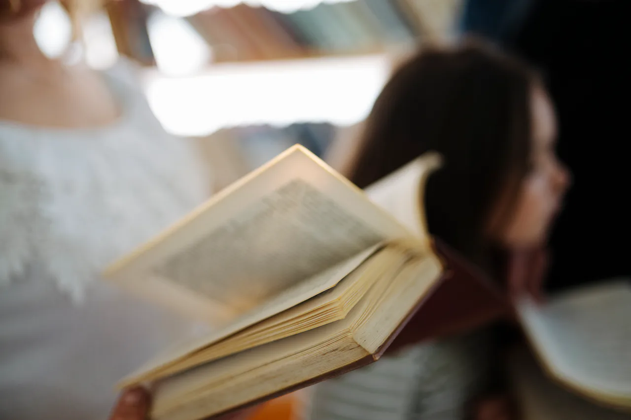 An open book in the foreground with people out of focus behind it in a library