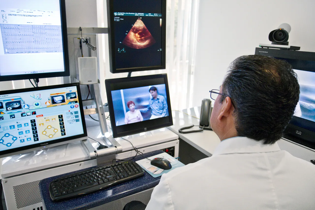 A doctor looks at screens and a video call during a telemedicine consultation.