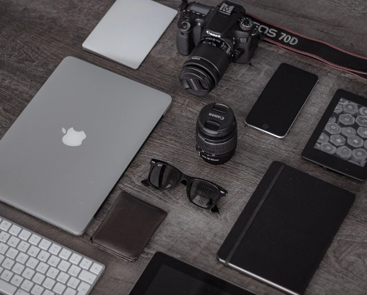 Camera, lenses, laptop, tablet and phones arranged on a table.