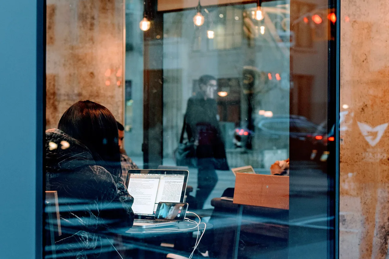 A person works on a laptop while making a video call on a phone.