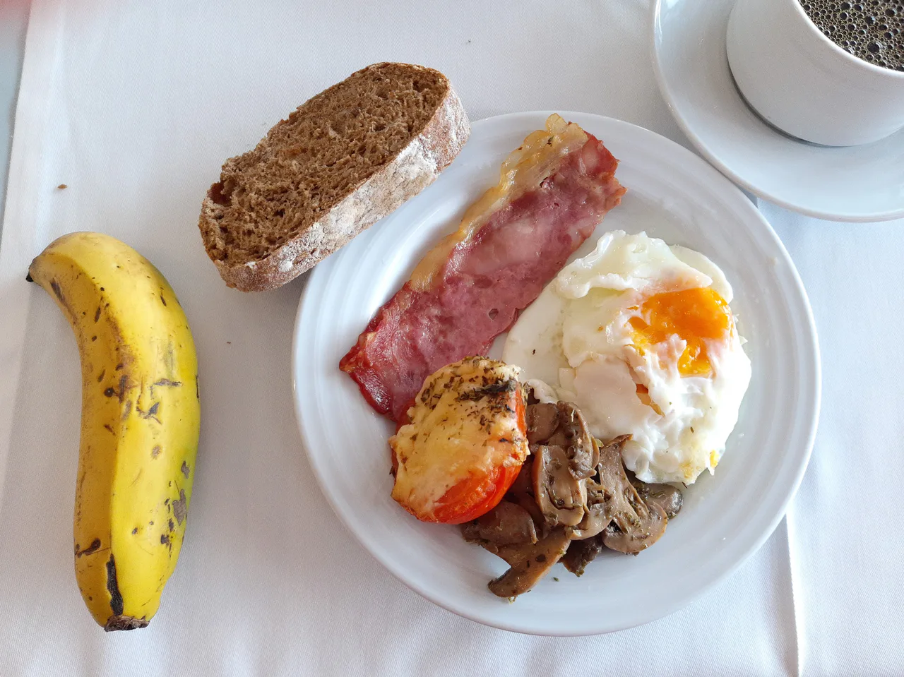 Desayuno de hotel con huevo, beicon, pan, fruta y café sobre un mantel blanco