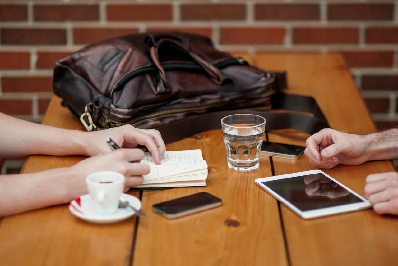 Dos personas intercambian información con teléfono y tableta sobre una mesa
