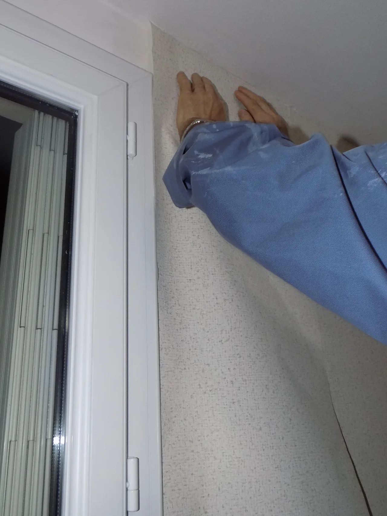 Manos colocando papel pintado texturizado junto a una ventana