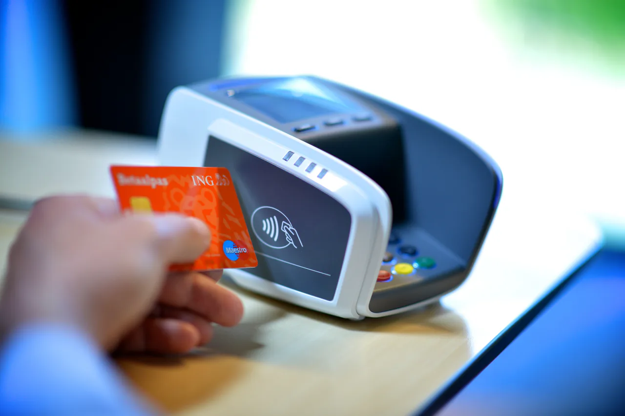 Una tarjeta de débito ING junto al lector de pago sin contacto de un terminal