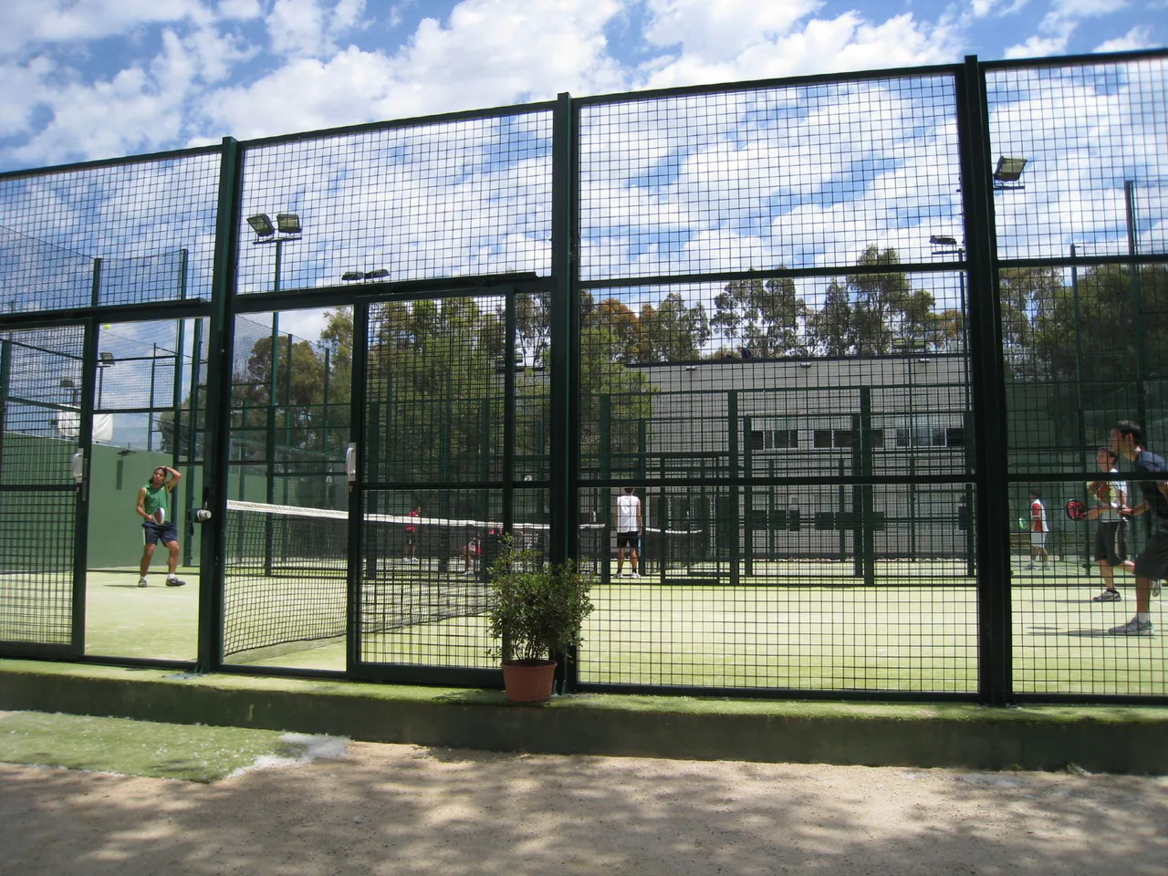 Players with padel paddles on an outdoor court surrounded by a metal mesh enclosure