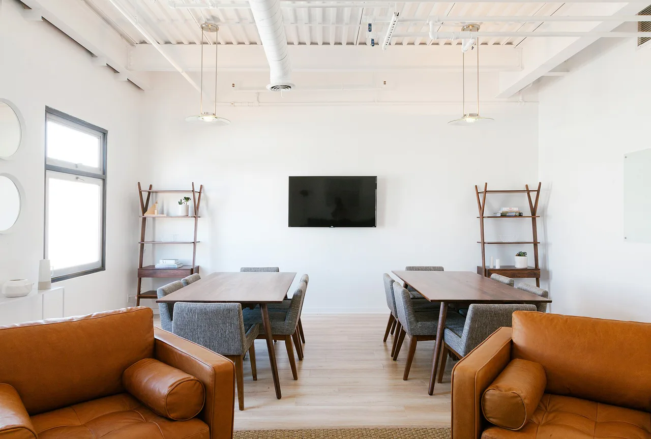 Sala de reunión con mesas, sillas y una pantalla