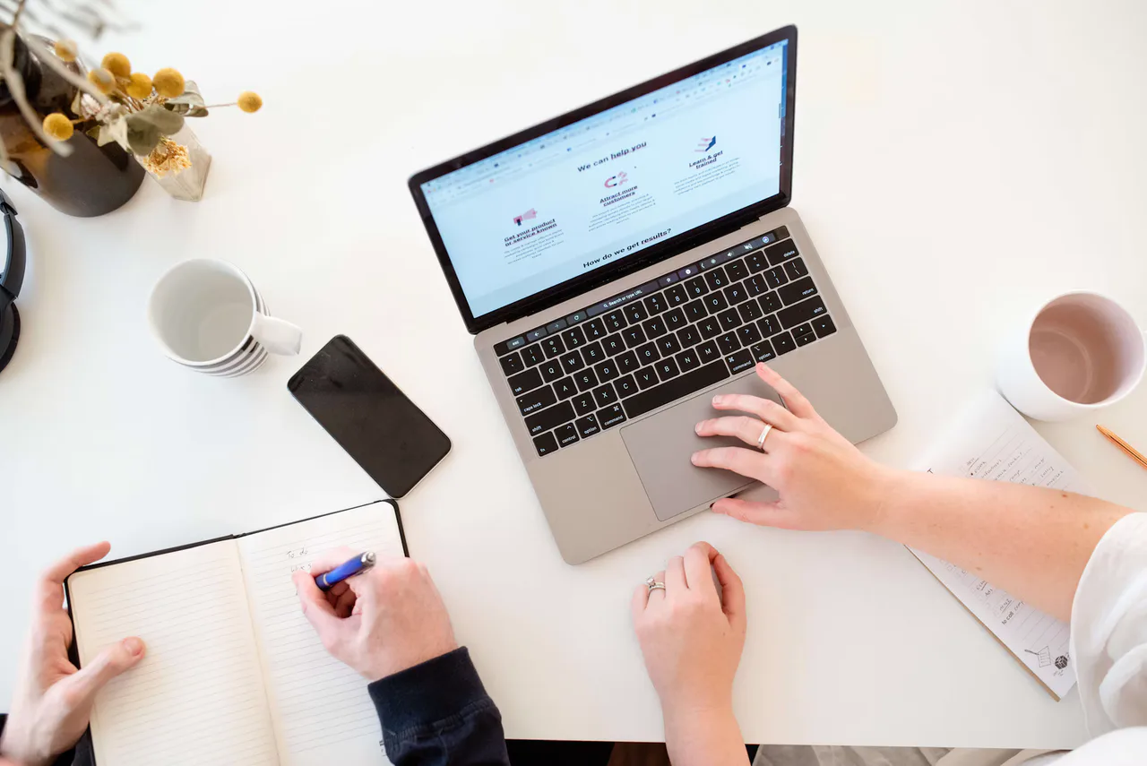 Dos personas revisan una web de marketing en un portátil junto a un cuaderno