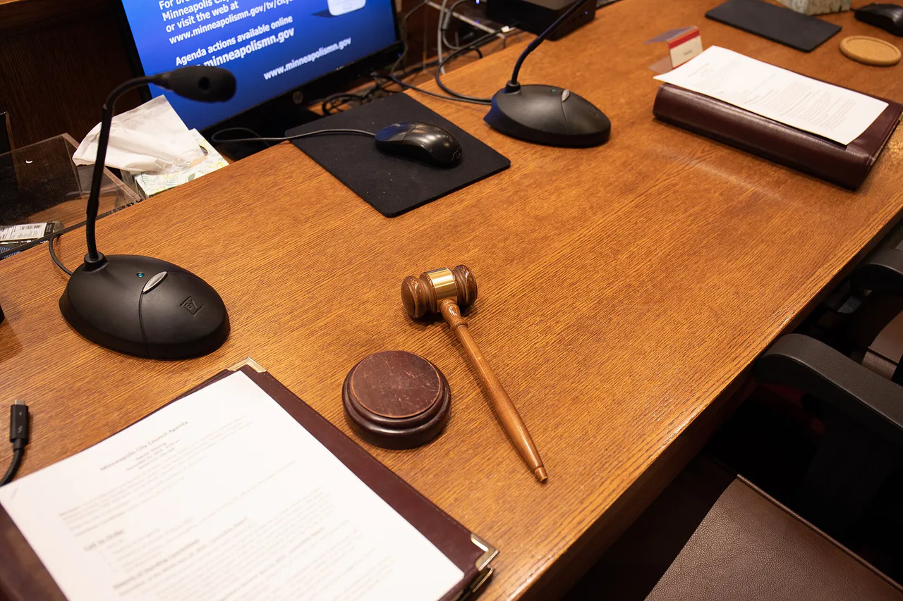 Una maza de presidencia está sobre la mesa de la sala del pleno, junto a micrófonos y documentos.