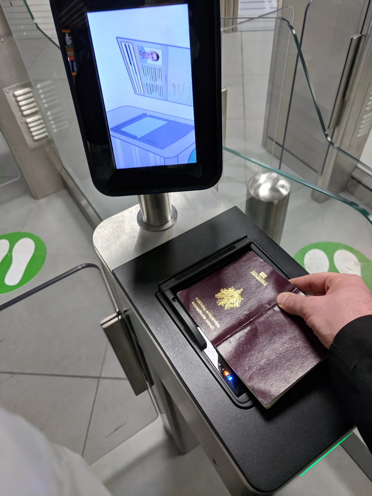 Una mano coloca un pasaporte en un lector bajo una pantalla de instrucciones.