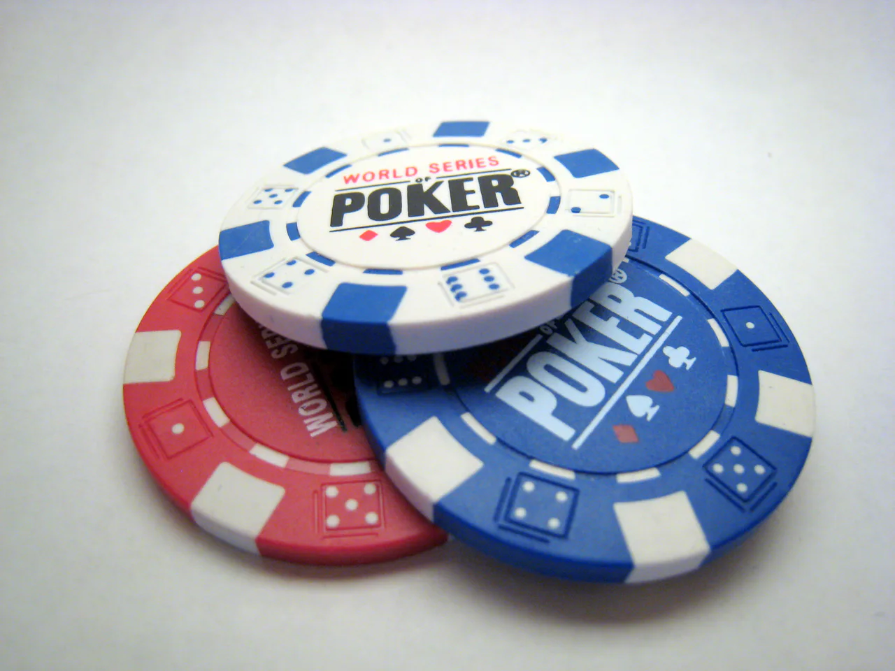 Tres fichas físicas de póker, dos azules y una roja, sobre una superficie clara.