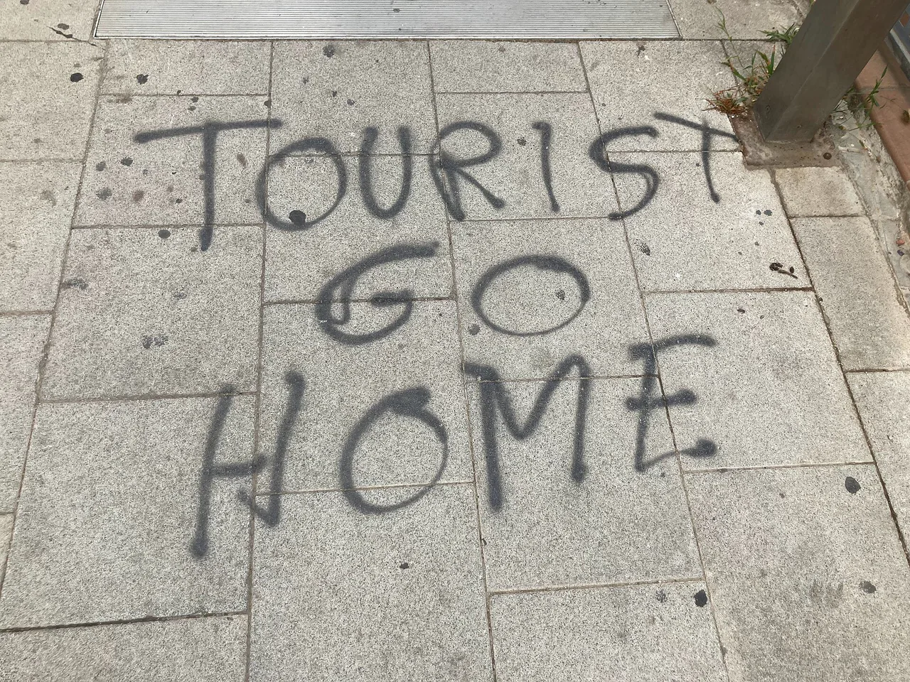 Pintada «TOURIST GO HOME» sobre una acera de Barcelona