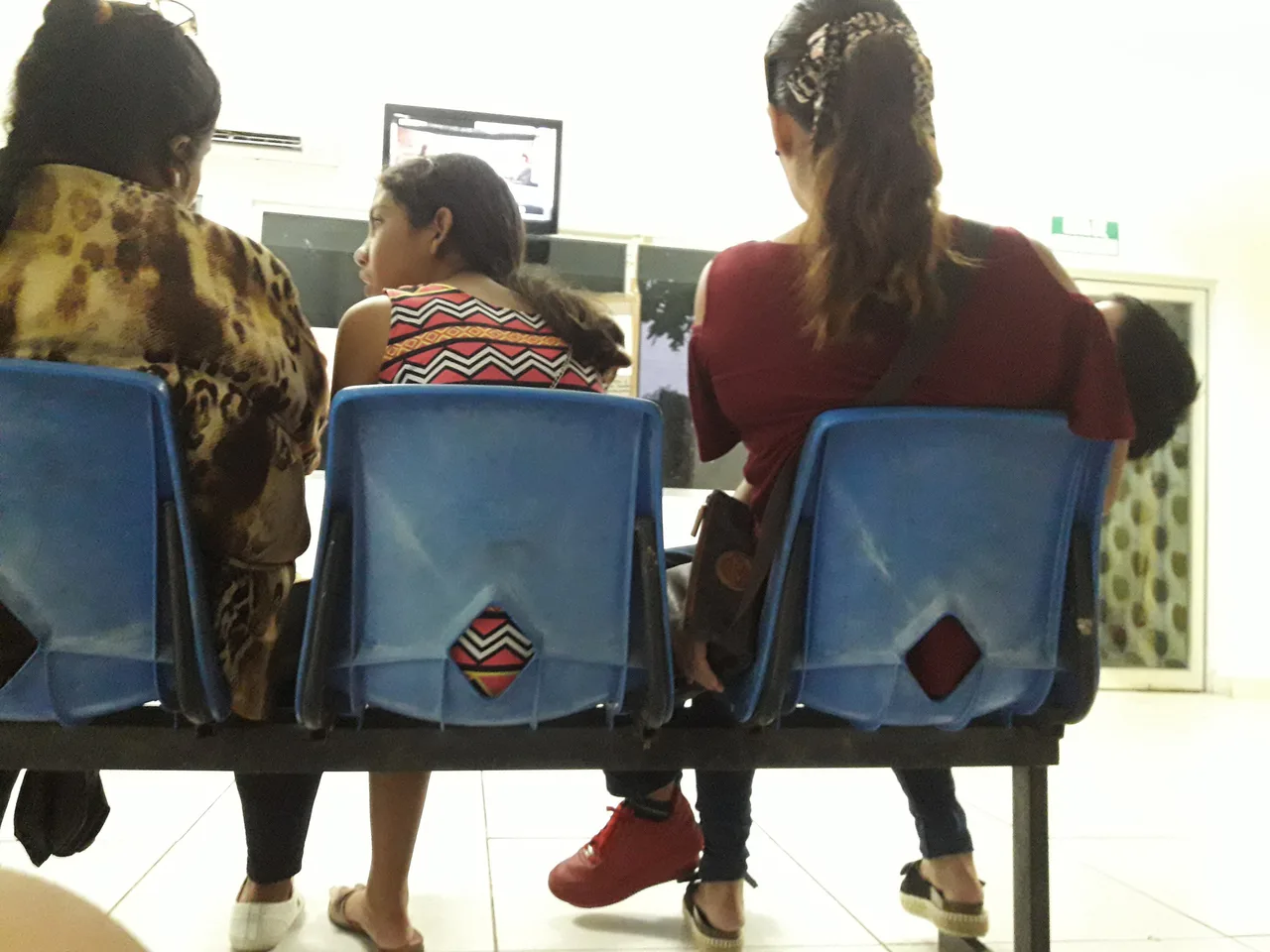 Varias personas sentadas en sillas azules de una sala de espera hospitalaria.