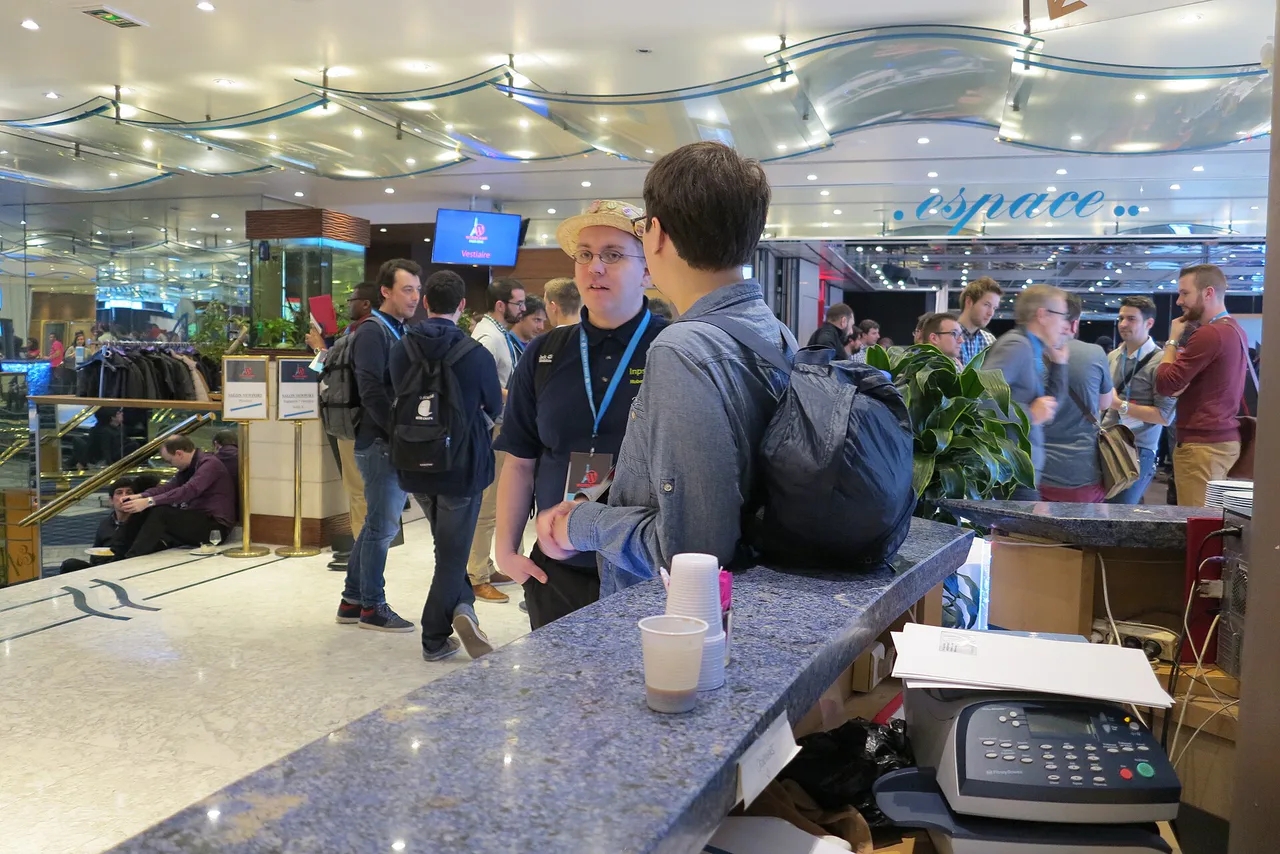 Several people wearing event badges talk in a conference reception area.