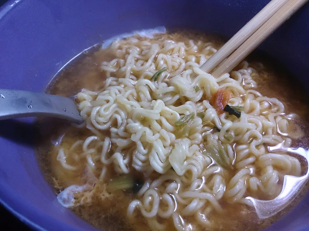 Instant noodles in a purple bowl with chopsticks and a spoon